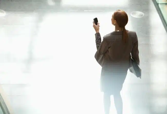 Businesswoman walking and looking down at cell phone