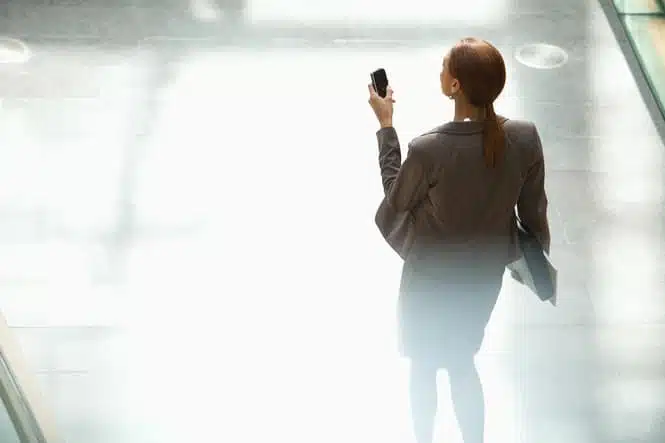 Businesswoman walking and looking down at cell phone